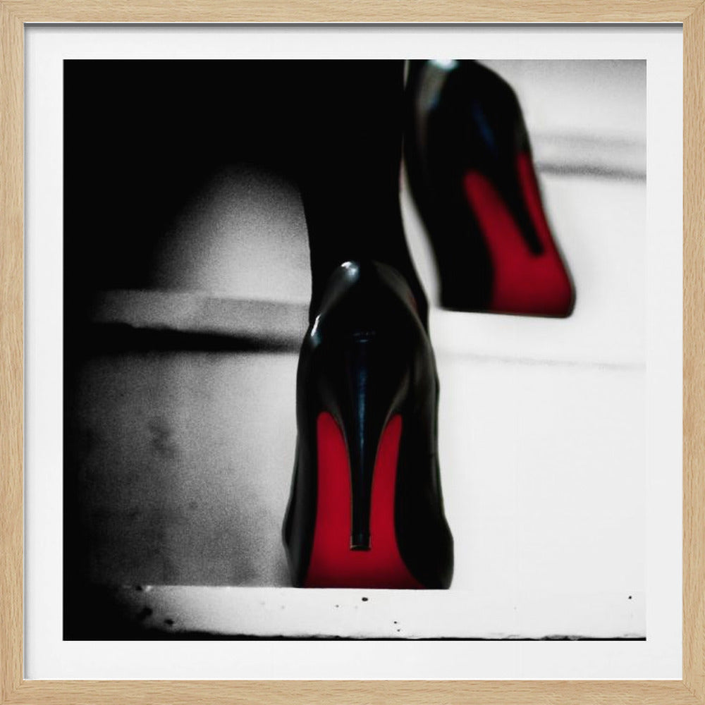A dramatic, low-angle, black and white photograph focusing on the back of a person wearing glossy black high heels with vibrant red soles, all set within a light wood frame. Artwork