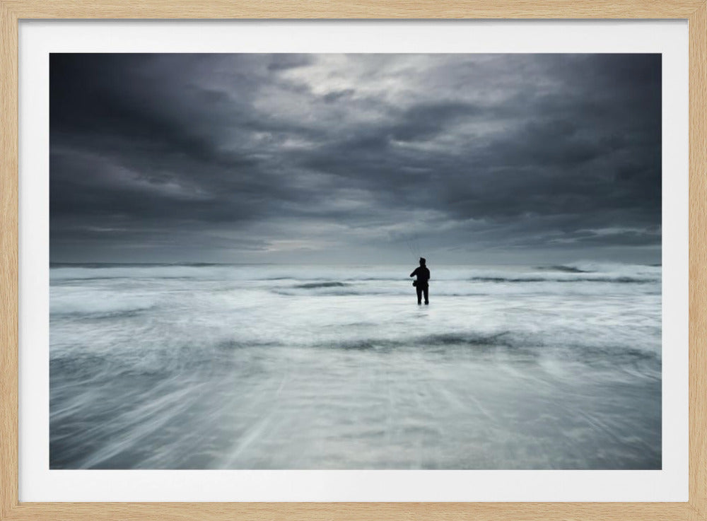 A moody, long-exposure photograph of a silhouetted fisherman standing in the churning white surf of the ocean under a dark, stormy sky, presented in a silver frame. Wall Art