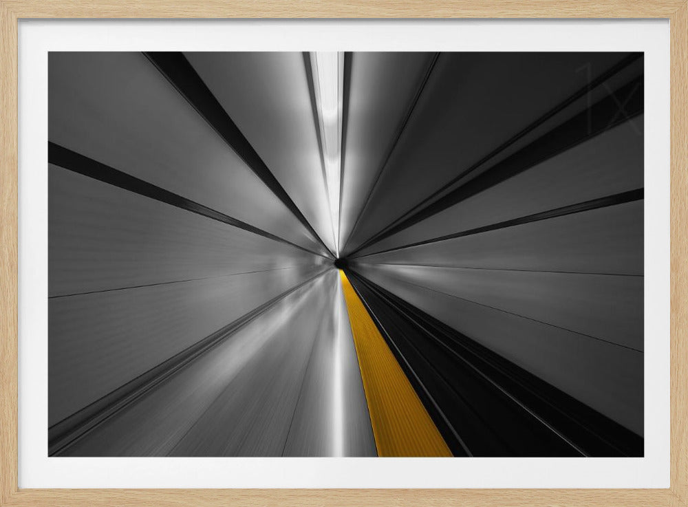 An abstract, long-exposure photograph from a first-person perspective inside a tunnel, creating a motion-blurred effect. The scene is mostly black and white, with lines radiating from a central vanishing point, but a single, bold yellow line runs down the center, adding a pop of selective color. The artwork is presented in a silver frame. Print