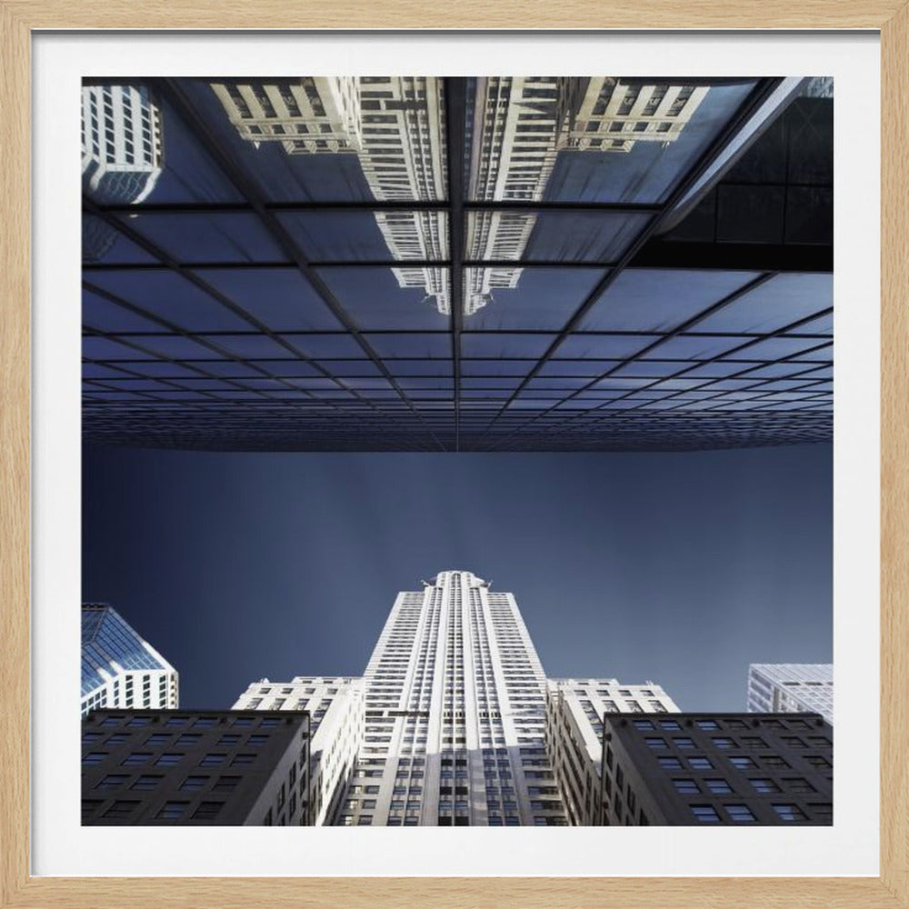 A framed, low-angle photograph capturing a stark white skyscraper against a deep blue sky, with its perfect reflection mirrored in the dark glass facade of an overhanging building, creating a surreal and symmetrical composition. Wall Art