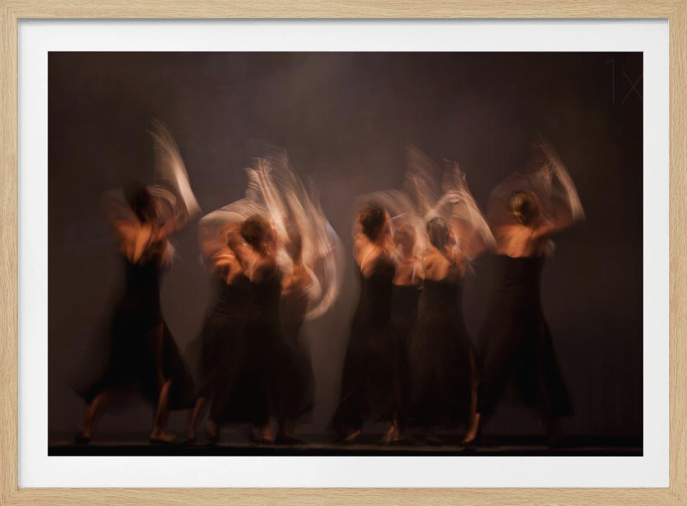 A long-exposure, artistic photograph capturing the fluid motion of dancers in black dresses against a dark brown background. The dancers' movements are rendered as ethereal, ghost-like blurs of light, conveying a sense of grace, energy, and rhythm. The image is presented within a silver frame. Wall Art
