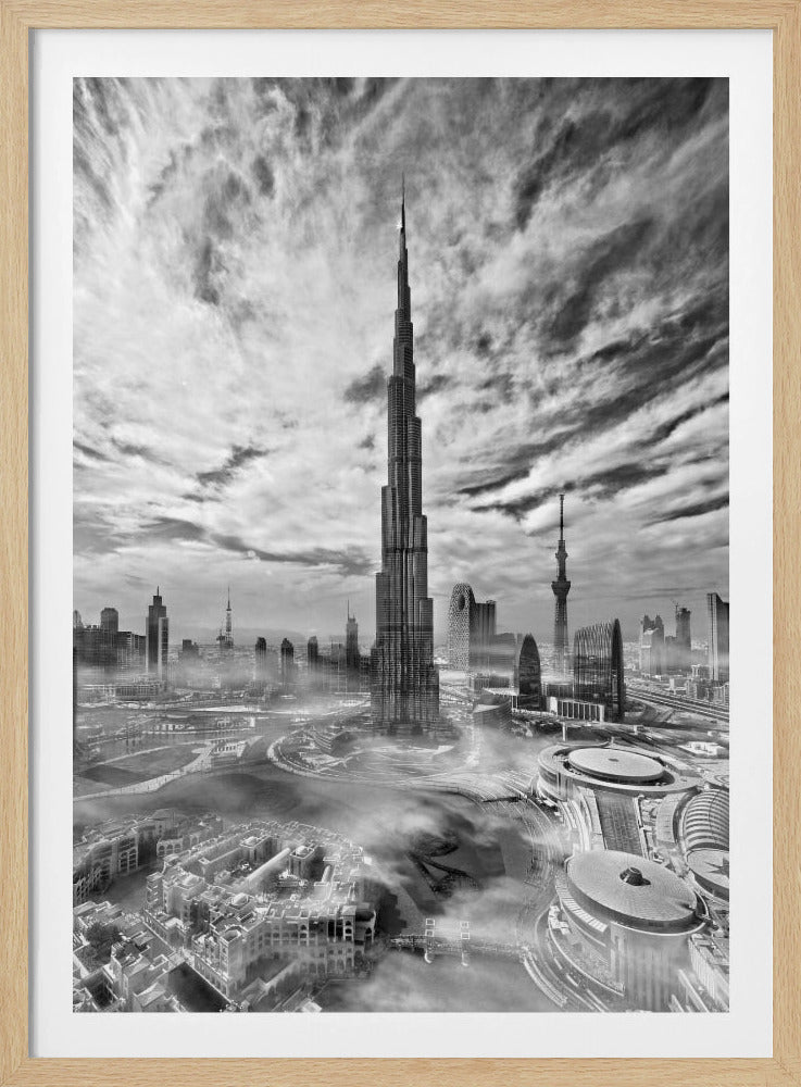 A dramatic black and white high-angle photograph of the Burj Khalifa dominating the Dubai cityscape, with swirling clouds above and a light mist surrounding the buildings below, all enclosed in a black frame. Poster