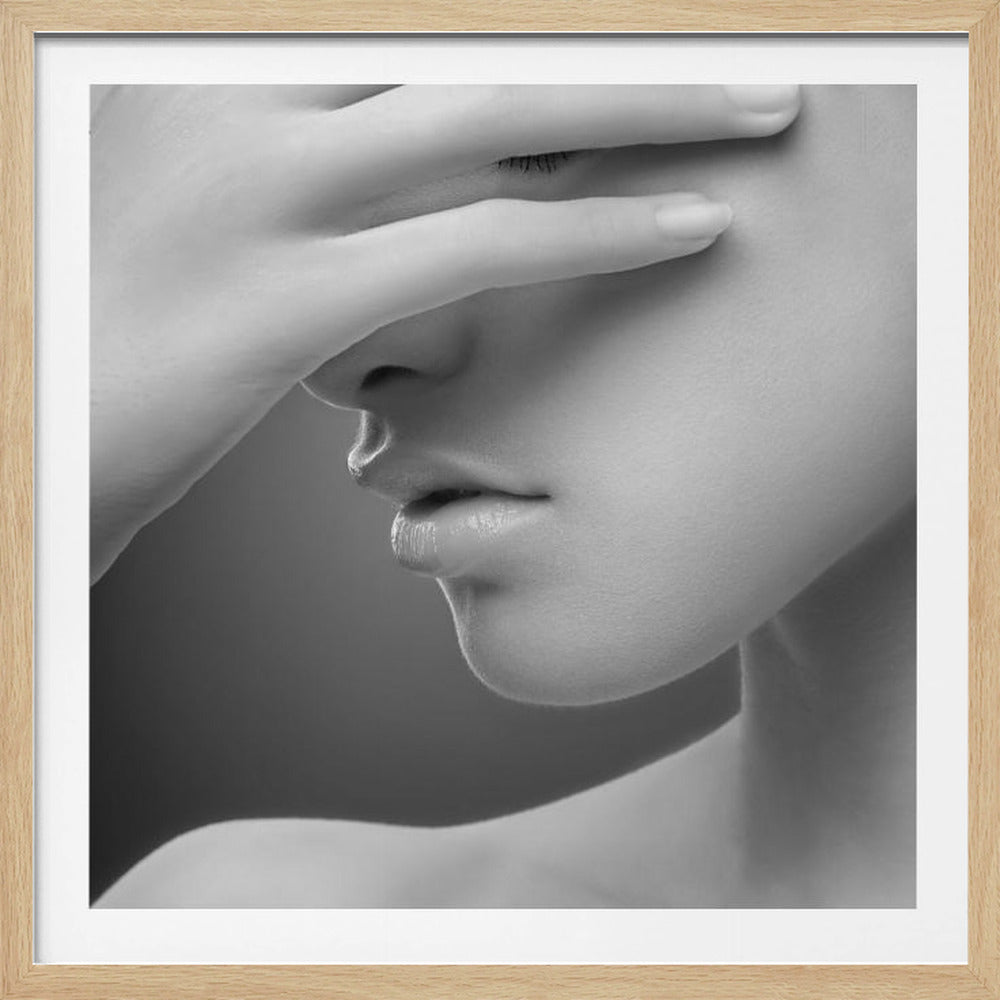 A close-up, black and white photograph of a woman's face. Her hand covers her eyes, revealing only the lower half of her face including her nose, lips, and chin. The image has a soft, sensual quality and is set within a light-colored wooden frame. Decor