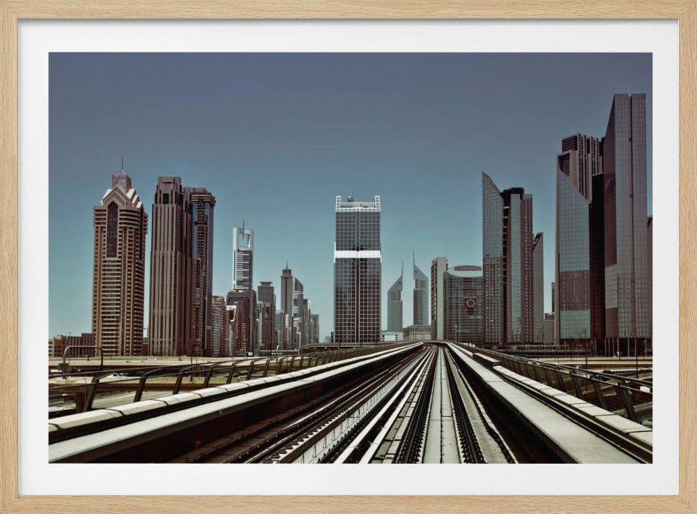 A view from an elevated train track looking down the rails towards the towering skyscrapers of a modern city skyline, under a clear, muted blue sky. Wall Art
