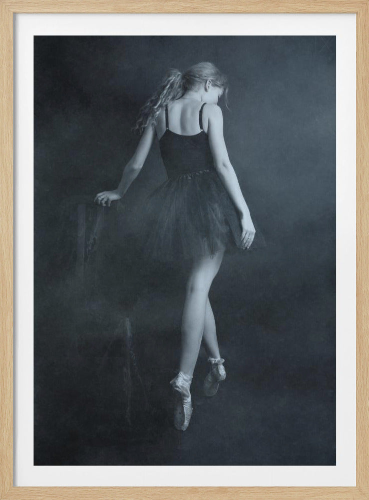 A moody, black and white photograph of a ballerina seen from behind. She wears a black leotard and tutu, with her blonde hair in a ponytail. She stands on pointe, her body turned slightly away from the viewer, against a hazy, dark background. Poster