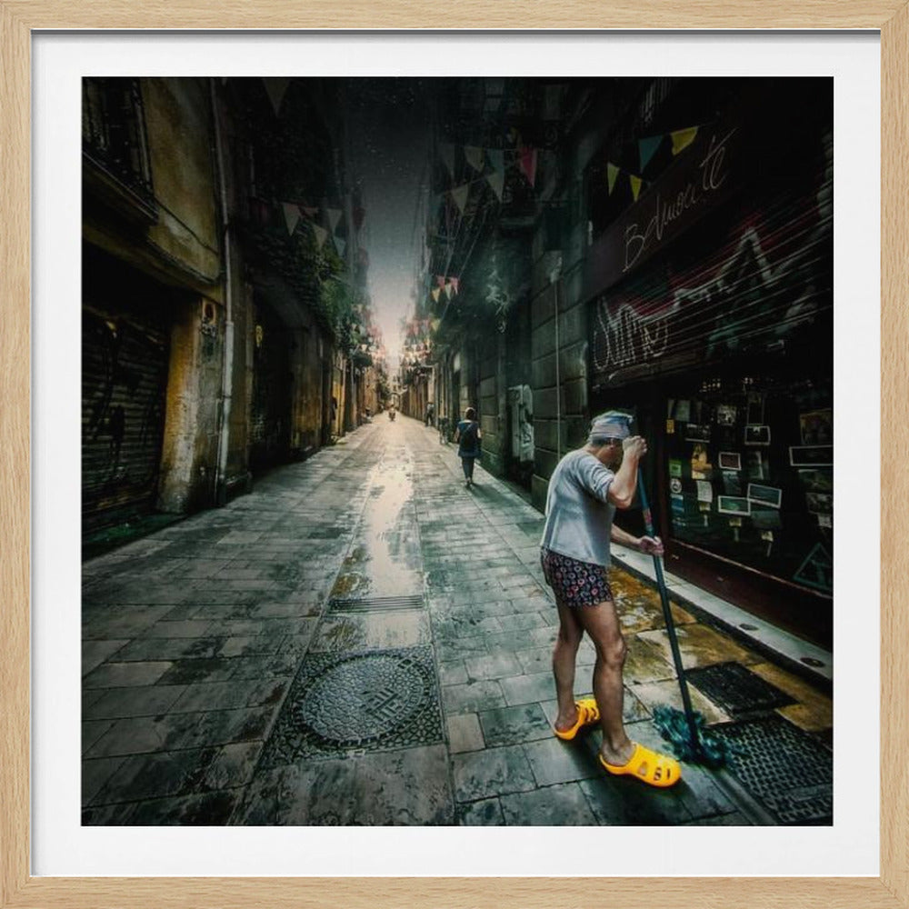 A wide-angle, atmospheric photograph of a man in bright yellow clogs mopping a wet, narrow cobblestone alley. The dark, gritty city street is lined with old buildings and closed storefronts, with another person walking in the distant light at the end of the alley. Wall Art