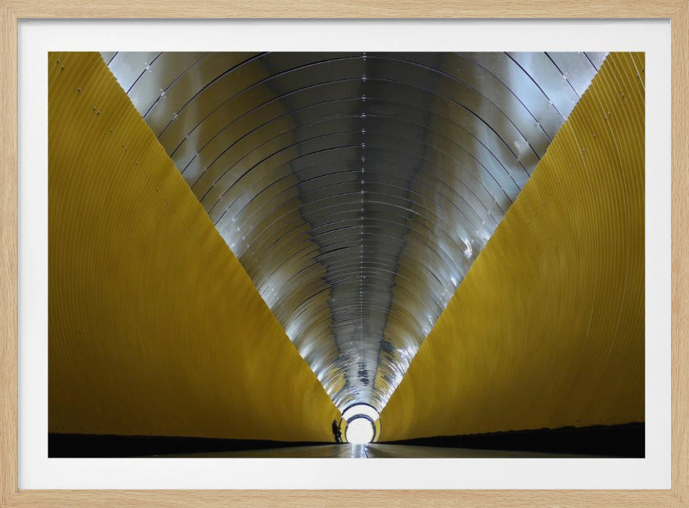 A symmetrical, perspective view down a modern, circular tunnel. The lower walls are bright yellow, creating two diagonal lines that converge towards a bright, white light at the far end. The arched ceiling is made of reflective silver metal panels, and a small silhouette stands near the exit. Artwork