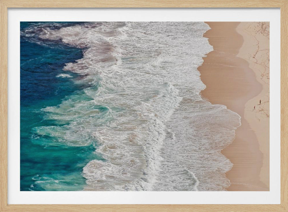 An aerial view of turquoise ocean waves with white foam crashing on a sandy beach where two small figures of people are walking, all framed in silver. Decor
