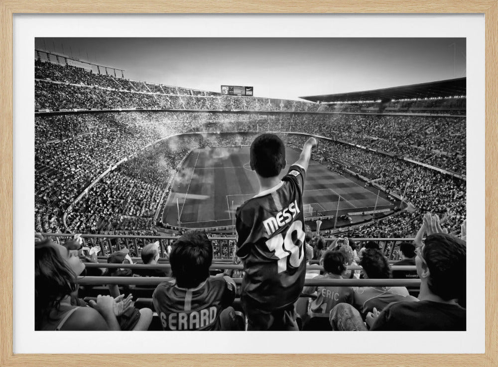 A framed, black and white photograph showing the back of a young boy wearing a 'MESSI 19' soccer jersey. He is standing in the upper stands of a massive, crowded stadium, pointing out towards the sunlit soccer field below. Other fans are visible around him, watching the game. Poster