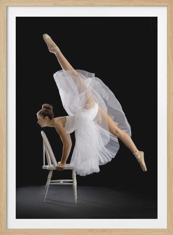 A graceful ballerina in a white tutu and pointe shoes performs a challenging vertical split while balancing on a white wooden chair against a solid black background, showcasing incredible strength and flexibility. Wall Art