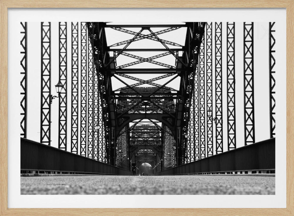 A framed, black and white, low-angle photograph capturing the symmetrical and intricate steel truss structure of a long bridge, creating a powerful vanishing point perspective down the center of the road. Poster
