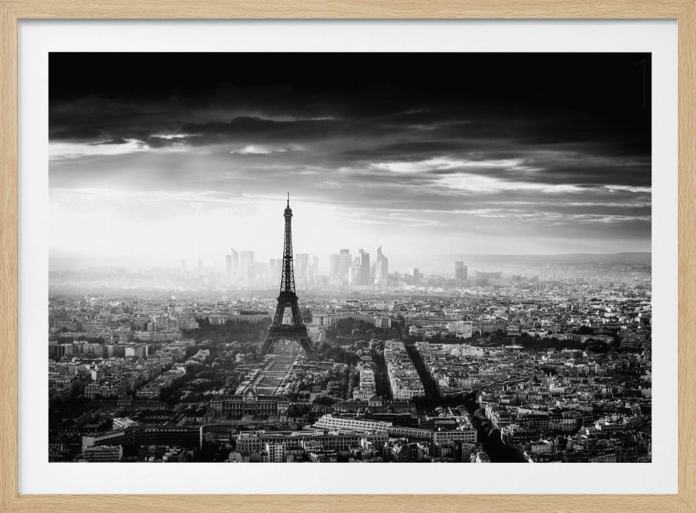 A dramatic black and white aerial photograph of Paris, showcased in a silver frame. The Eiffel Tower is the central focus, standing tall amidst the sprawling cityscape. In the background, a modern skyline is visible through a light haze, all under a dark, moody, and cloudy sky. Artwork
