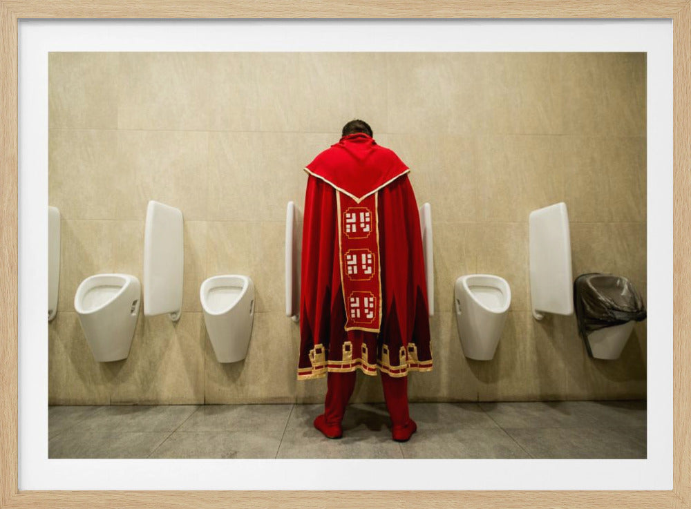 A back view of a person wearing an elaborate, long red and gold cape, standing at a urinal in a modern public restroom with beige tiled walls and multiple white urinals. Artwork