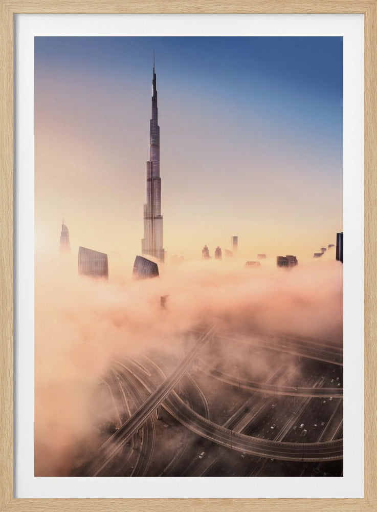 An aerial photograph of the Burj Khalifa in Dubai, towering over a thick blanket of pink and orange-hued fog at sunrise. Below the fog, a complex highway interchange is visible, with the clear blue sky above. Wall Art