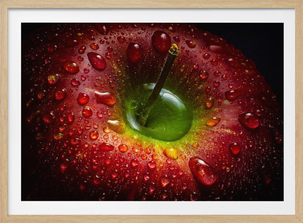 A dramatic macro shot of a wet red apple, with glistening water droplets covering its skin. The stem is in the center, emerging from a bright green hollow, contrasting with the deep red and dark background. The image is presented in a silver frame. Poster