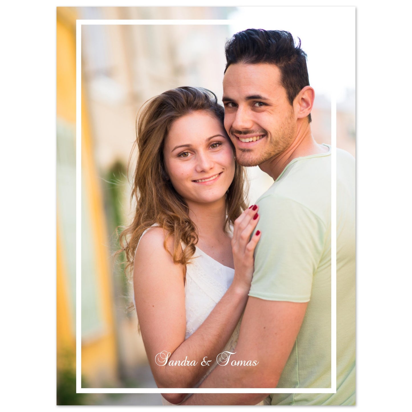 A vertical photograph of a smiling young couple embracing outdoors. The man has dark hair and wears a light green shirt, while the woman has long brown hair and wears a white top. The photo is framed with a thin white border, and the names 'Sandra & Tomas' are written in elegant white script at the bottom. Poster