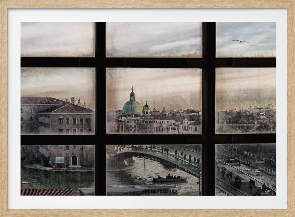 A view of the Venice cityscape through a dark, multi-paned window. Below, people cross a modern bridge over a canal with boats, while in the distance, the green domes of a historic church rise above the surrounding buildings. The photo has a muted, vintage feel and is presented in a silver frame. Print