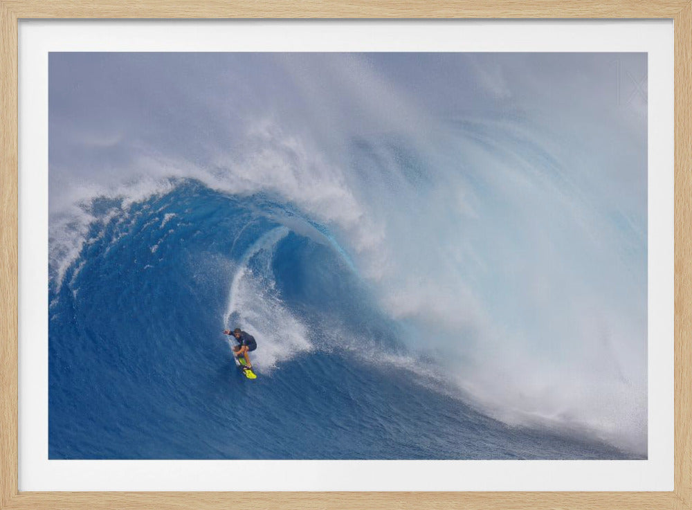 A framed photograph of a professional surfer skillfully riding down the steep face of a massive, cresting blue ocean wave, surrounded by white sea spray. Decor