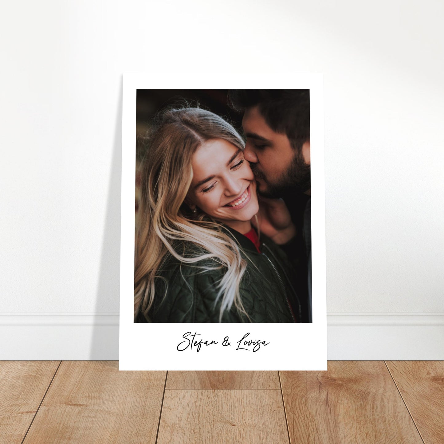 A polaroid-style poster featuring a close-up photograph of a bearded man kissing a smiling blonde woman on the cheek. She has her eyes closed and is wearing a green jacket. Below the photo, on the white border, the names 'Stefan & Lovisa' are written in a black script font. Wall Art