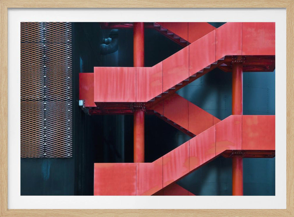 A framed abstract architectural photograph of a bright red industrial staircase zig-zagging against a dark teal wall. The composition highlights the geometric shapes and bold color contrast between the red stairs and the cool-toned background, with a silver mesh panel visible on the left side. Print