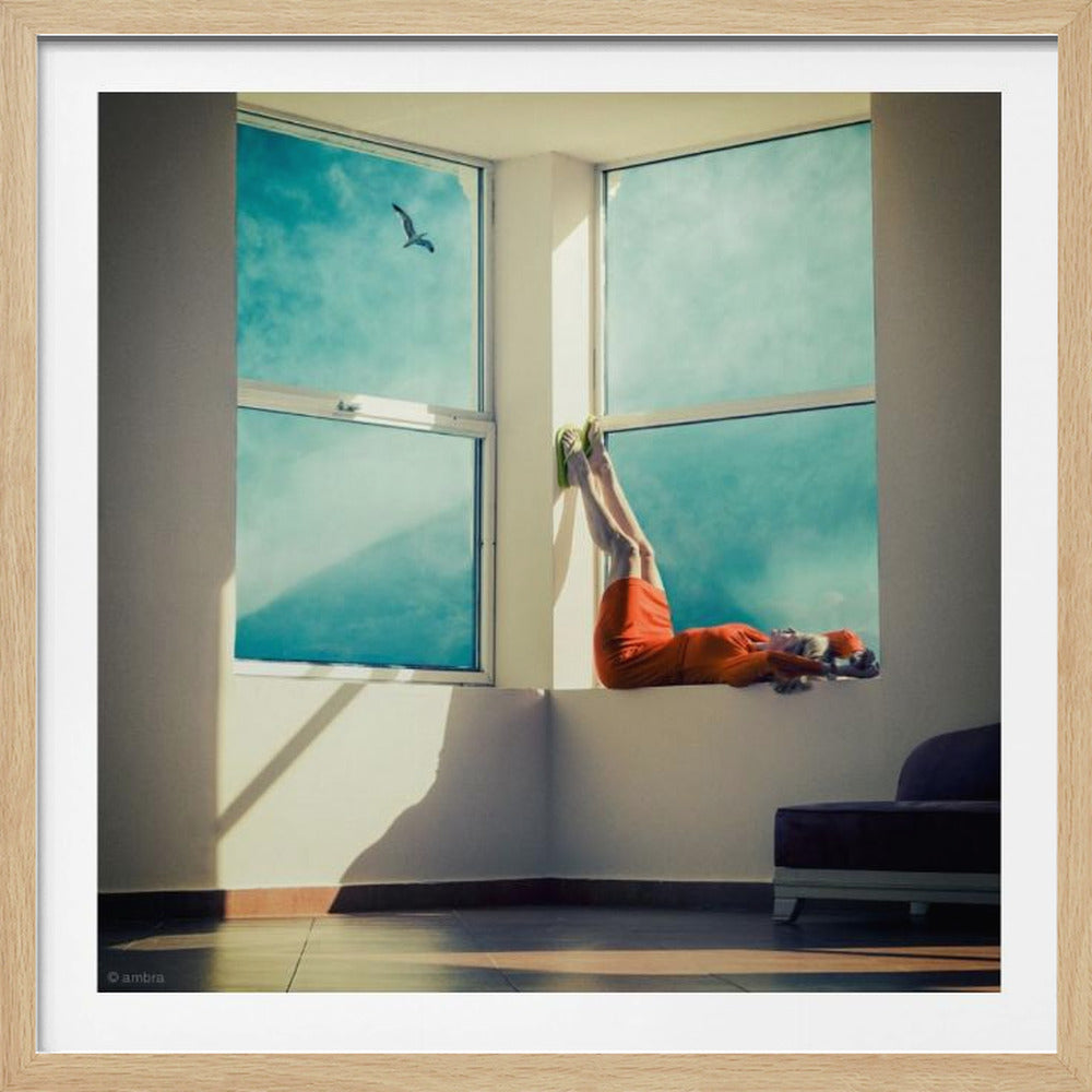 A surreal photograph of a woman in a bright orange dress lying on a wide, sunlit windowsill with her legs up against the wall. Through the large windows, a single bird is seen flying in a vibrant teal sky. The image, presented in a light wood frame, captures a moment of quiet contemplation and escape. Wall Art