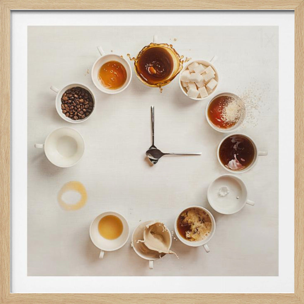 A creative flat lay photograph of a clock made from coffee cups and ingredients. Twelve white cups are arranged in a circle on a white background, each representing an hour and filled with different coffee-related items like beans, honey, sugar cubes, and various stages of coffee with milk splashing. In the center, two silver spoons form the hands of the clock. The entire image is presented within a light wood frame. Decor