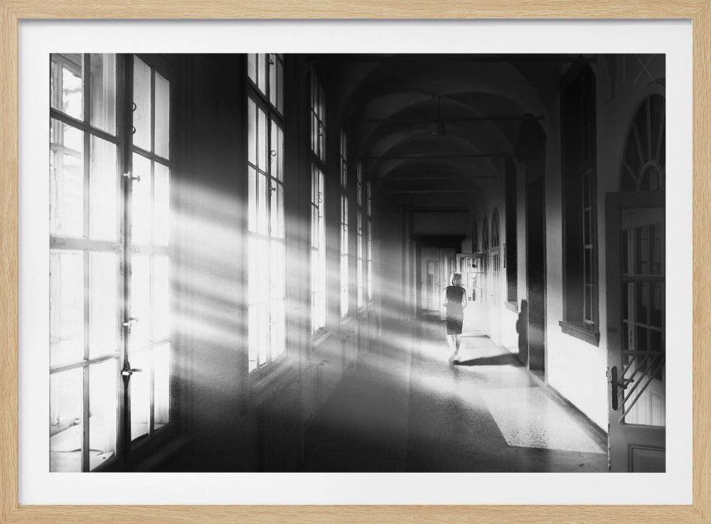 A black and white photograph of a woman walking away down a long, dark hallway. Bright shafts of sunlight pour through large windows on the left, creating a dramatic interplay of light and shadow on the floor and walls. Poster
