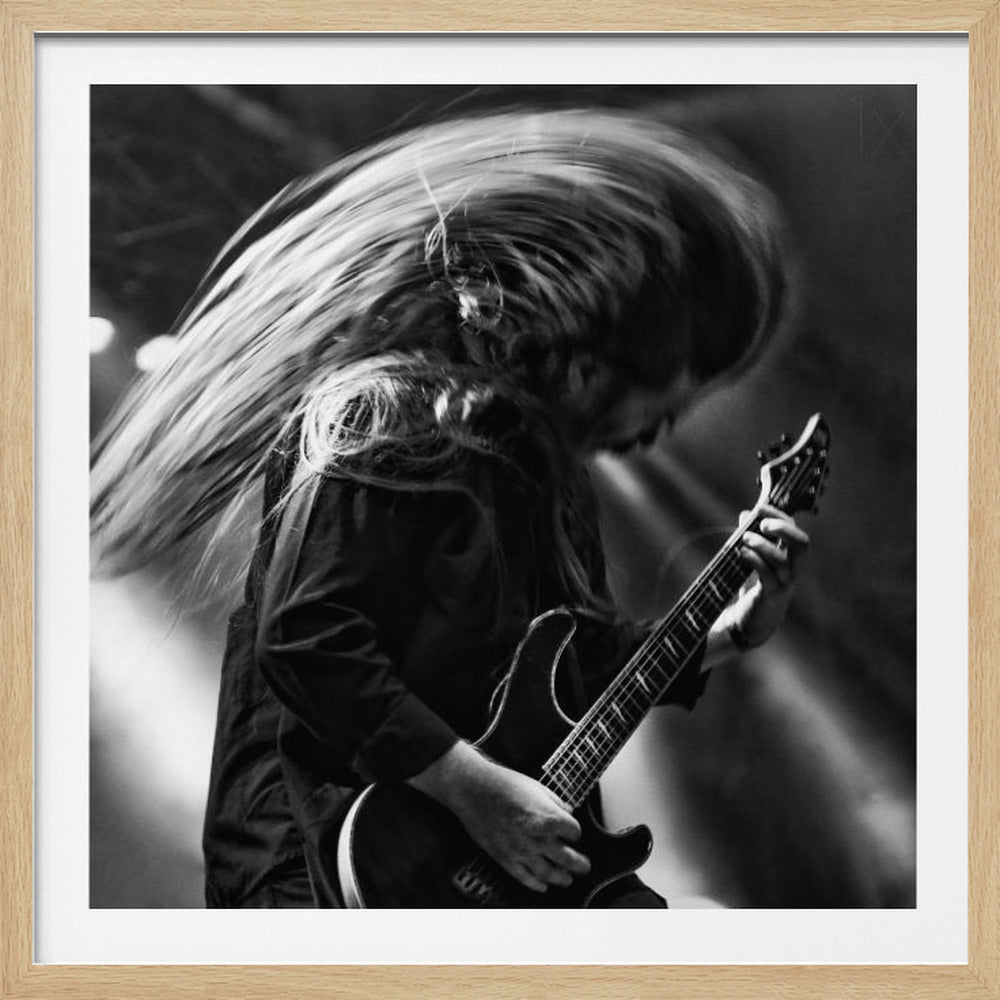 A dynamic black and white action shot of a long-haired guitarist headbanging while playing an electric guitar on stage. Their hair is a dramatic motion blur, conveying intense energy and movement during a live performance. Wall Art