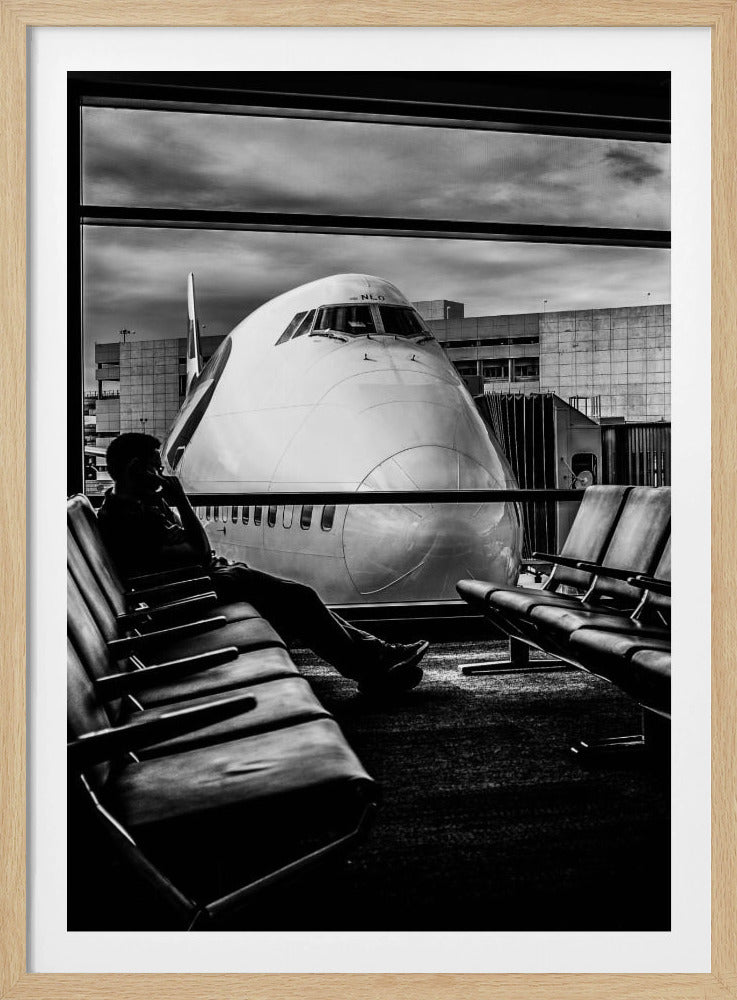 A dramatic black and white photograph of a silhouetted person sitting in an airport departure lounge, waiting for their flight. Through the large window, the enormous nose of a Boeing 747 jumbo jet is visible up close, dominating the view under a cloudy sky. Artwork