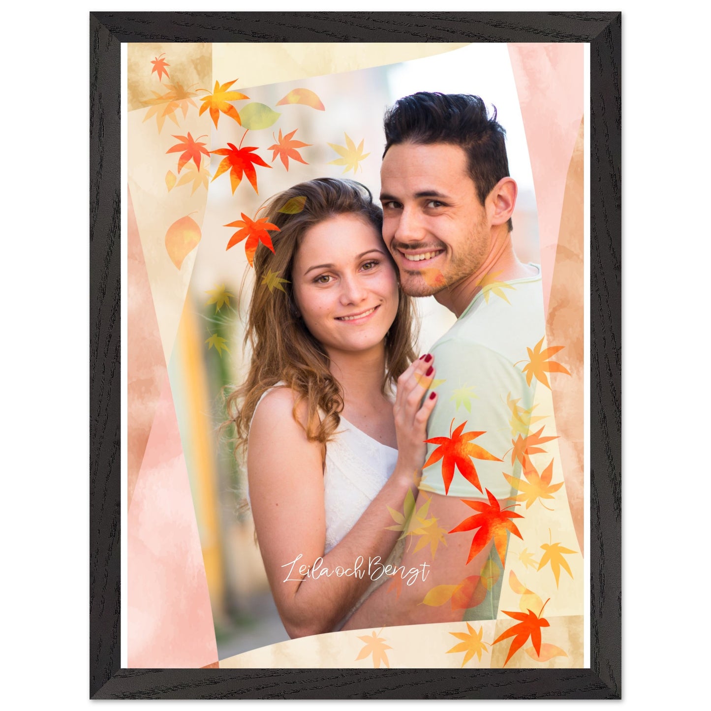 A framed portrait of a smiling couple, Leila and Bengt, hugging. The image is overlaid with a decorative autumn theme featuring red and orange maple leaves and soft pink and beige geometric shapes. The piece is set within a black wood-grain frame. Decor