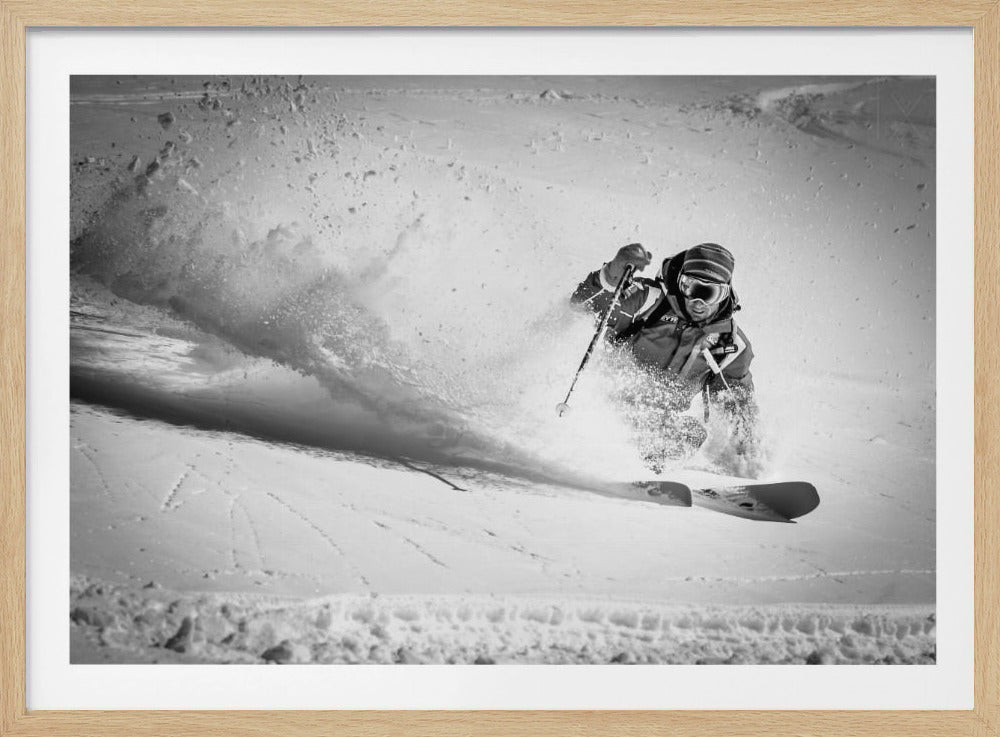 A framed, black and white action shot of a skier making a sharp turn on a snowy slope, sending a large spray of powder into the air. The skier is leaning into the turn, fully kitted out in winter gear including goggles and a beanie. Artwork