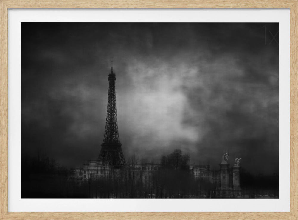A moody, atmospheric black and white photograph of the Eiffel Tower in Paris. The tower stands against a dark, cloudy sky, creating a dramatic and artistic impression. The image is presented within a brushed silver frame. Artwork