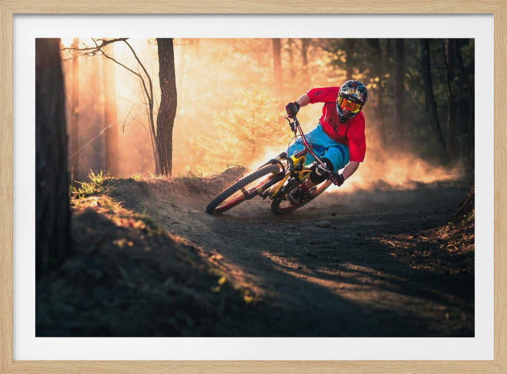 A mountain biker in a red shirt, blue shorts, and full-face helmet leans sharply into a dusty turn on a dirt trail in a forest. The setting sun casts a warm, golden light through the trees, creating a dramatic, backlit effect. Wall Art