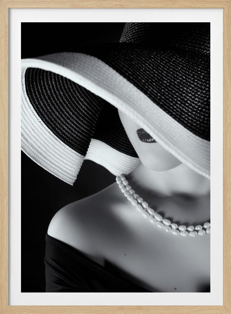 A glamorous black and white close-up photo of a woman wearing a large, striped sun hat that hides her eyes, revealing only her dark lips. She wears a pearl necklace and an off-the-shoulder top against a dark background, creating a mysterious and elegant mood. Wall Art