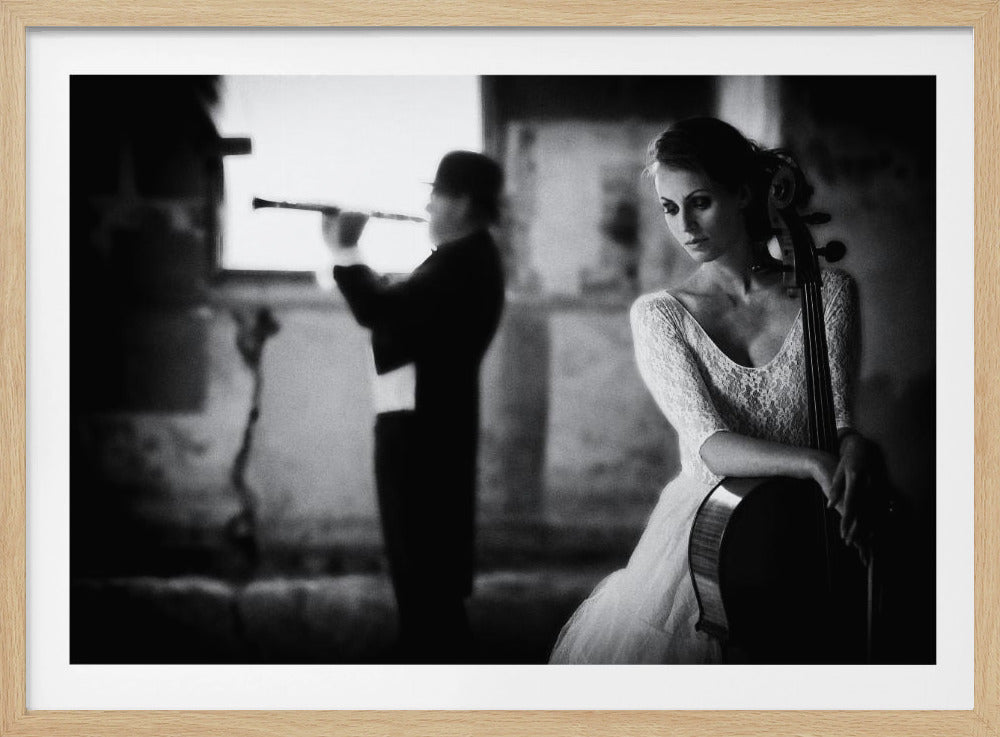 A moody, black and white photograph of a woman in a white lace dress holding a cello, with a man in silhouette playing a flute in the background, all enclosed in a silver frame. Print
