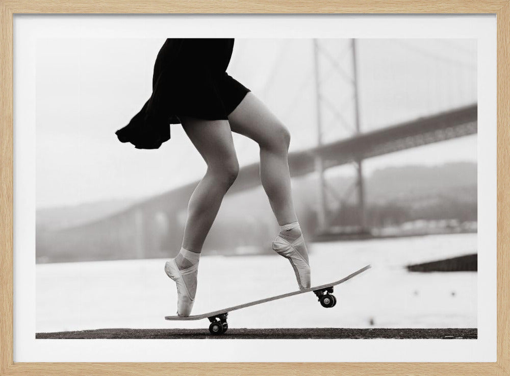 A black and white photograph of a ballerina's legs in a black dress, balancing en pointe on a skateboard with a blurred bridge in the background. Artwork