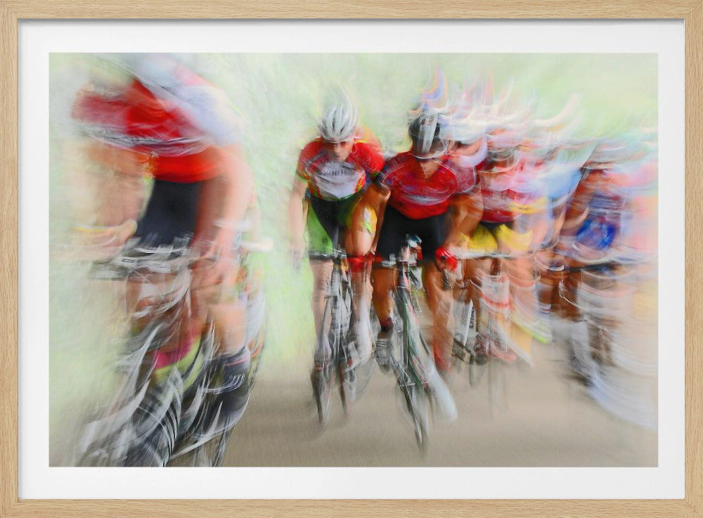 An abstract photograph of a group of cyclists in a race, captured with motion blur to create a dynamic sense of speed. The riders' red jerseys and the green background are streaked together, with a silver frame surrounding the image. Artwork