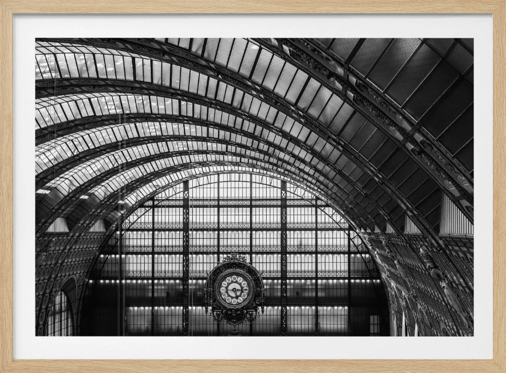 A black and white photograph capturing the grand, arched ceiling of the Musée d'Orsay in Paris. The intricate ironwork and glass panels of the former train station curve across the frame, leading the eye to the iconic, ornate clock against a massive windowed wall. Wall Art