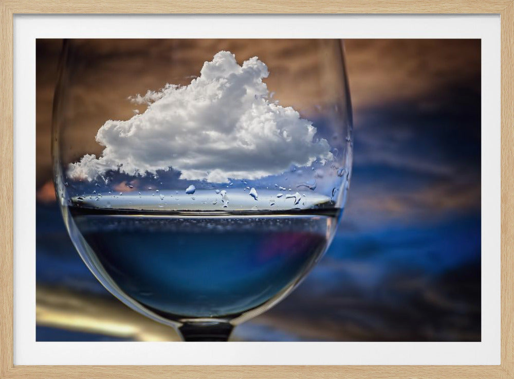 A surreal close-up of a wine glass holding blue liquid and a single white cloud, with water droplets on the glass, set against a blurred background and enclosed in a silver frame. Print