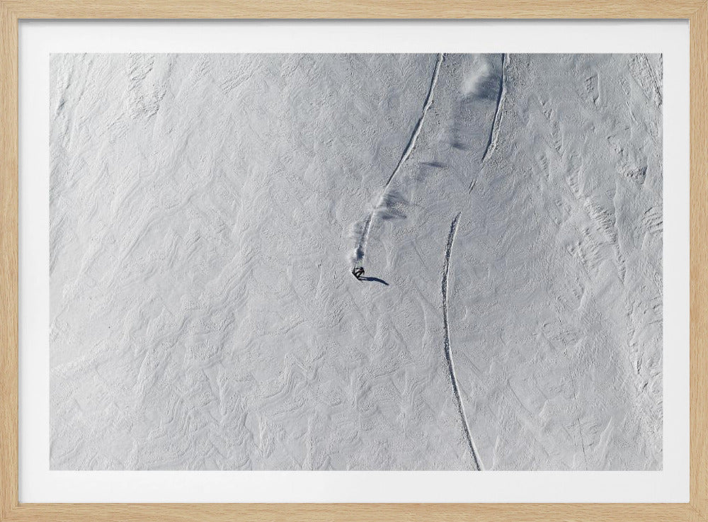 An aerial, top-down photograph of a lone snowboarder carving a turn down a vast, textured, snowy mountain slope, leaving fresh tracks in the powder. The image is presented in a simple, grey frame. Wall Art