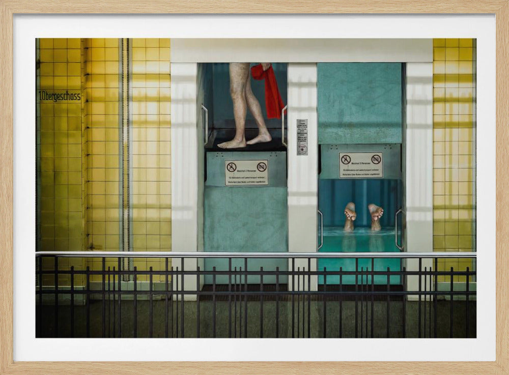 A surreal, framed artwork depicting two teal-colored vertical cabins against a yellow tiled wall. In the left cabin, a person's bare legs are visible as they hold a red towel. In the right cabin, which is filled with water, only a pair of feet can be seen submerged. A black railing is in the foreground, adding to the strange, layered composition. Artwork