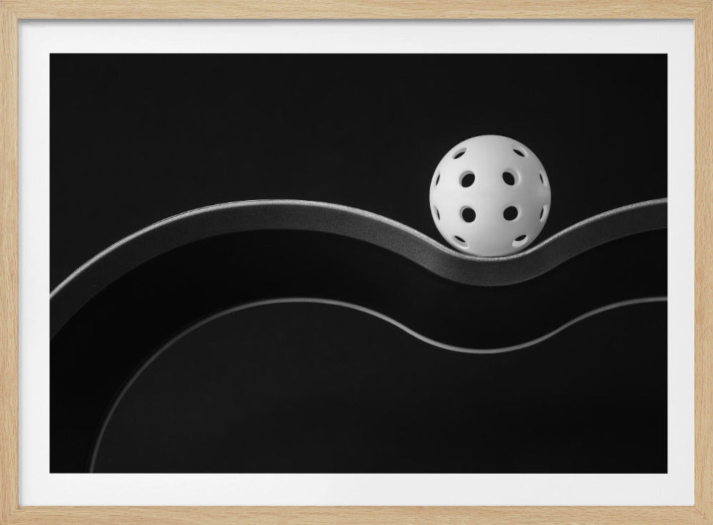 A minimalist black and white photograph of a white pickleball resting perfectly balanced on a thick, wavy, textured line against a solid black background. Below it, a thin white line mimics the curve. The entire piece is framed in silver. Poster