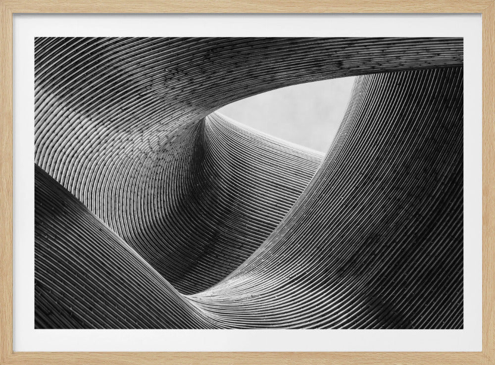 A framed, black and white abstract photograph of a swirling, textured structure. The low-angle shot looks up at curving walls made of thin, parallel lines, creating a dynamic sense of movement and depth, with an opening to a bright sky at the top. Artwork