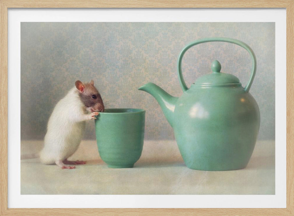 A small, white and brown hooded rat stands on its hind legs with its front paws on the rim of a green teacup, appearing to look inside. To the right is a matching green teapot, all set against a soft, pale blue patterned background and presented in a silver frame. Decor
