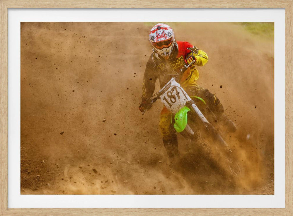 An action shot of a motocross rider in full red and yellow gear, speeding through a dirt track and kicking up a large cloud of brown dust and debris. Print