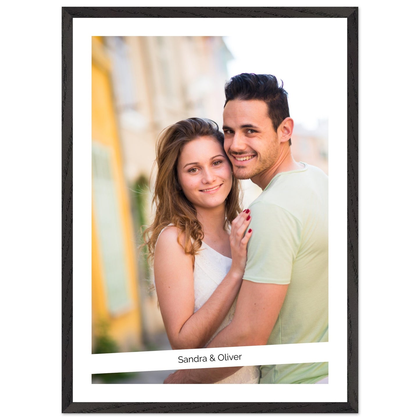 A personalized framed photo of a smiling young couple, Sandra & Oliver, embracing outdoors. The photo has a white border and is set within a black wood-textured frame. Decor