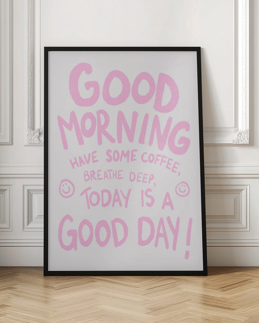A framed art print with a positive message written in a casual, hand-drawn pink font on a white background. The text reads 'GOOD MORNING HAVE SOME COFFEE, BREATHE DEEP, TODAY IS A GOOD DAY!' and is accented with two small smiley faces. Print