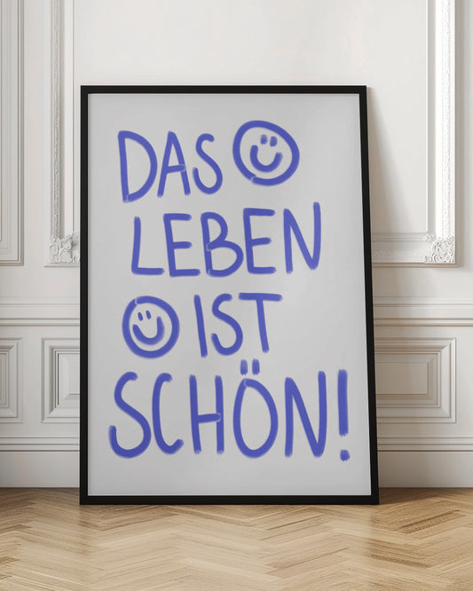A typography poster in a black frame with the German phrase 'Das Leben ist schön!' handwritten in a playful blue font on a white background. The letter 'O' in 'DAS' is replaced with a smiley face, and another smiley face is drawn before the word 'IST'. Poster