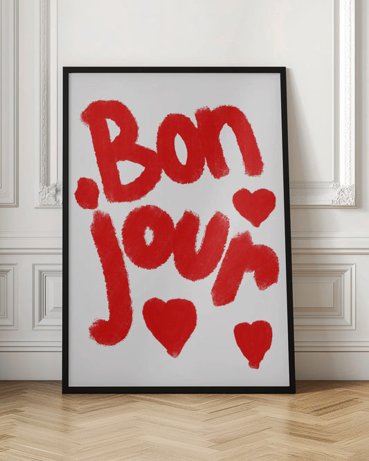 A minimalist art print featuring the French greeting 'Bonjour' written in a bold, textured red script. The text is surrounded by three hand-drawn red hearts on a clean white background, all framed in black. Wall Art