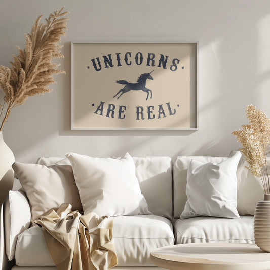 A framed art print with a cream background featuring the phrase 'UNICORNS. 'ARE REAL.' in a dark navy, vintage-style font. Between the words, there is a silhouette of a leaping unicorn. Print